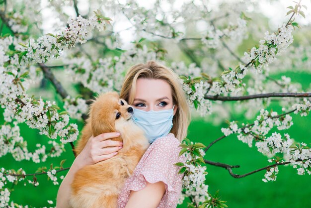 Jeune femme et spitz rouge avec un masque médical sur son visage sur la nature un jour de printemps