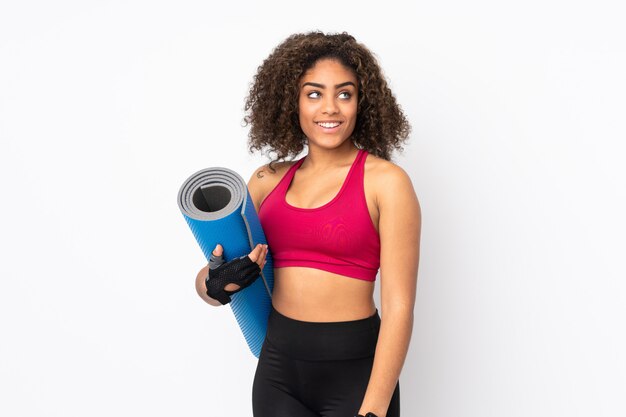 Jeune femme de sport afro-américaine isolée sur blanc avec un tapis et souriant