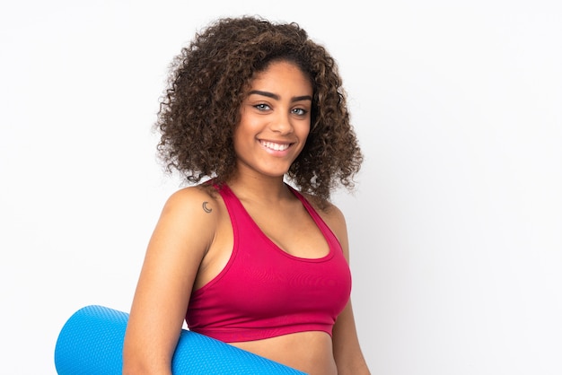 Jeune femme de sport afro-américaine isolée sur un espace blanc avec un tapis et souriant