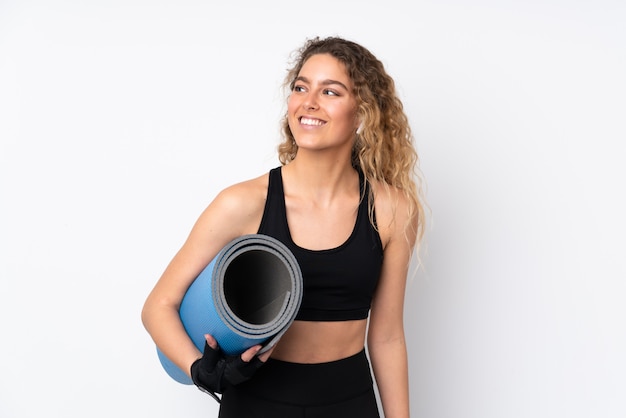 Jeune femme sport isolée sur mur blanc avec un tapis et souriant