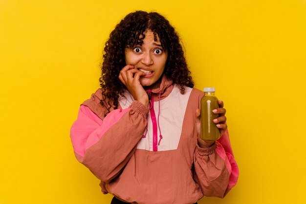 Jeune femme de sport métisse tenant un smoothie isolé sur mur jaune