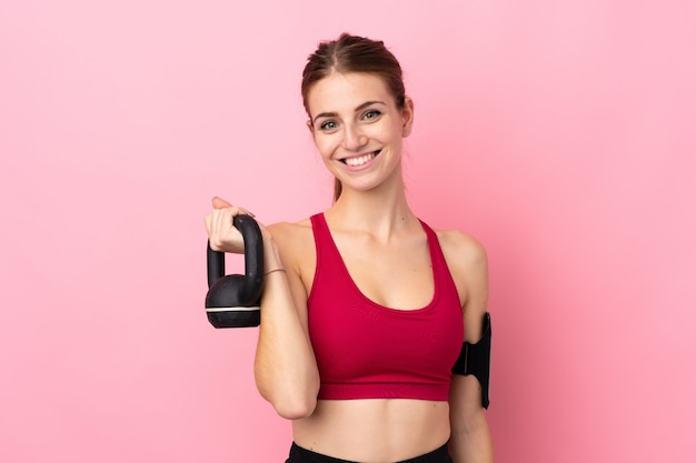 Jeune femme sport sur mur rose isolé faisant de l'haltérophilie avec kettlebell