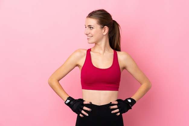 Jeune femme sport sur mur rose isolé posant avec les bras à la hanche et à côté