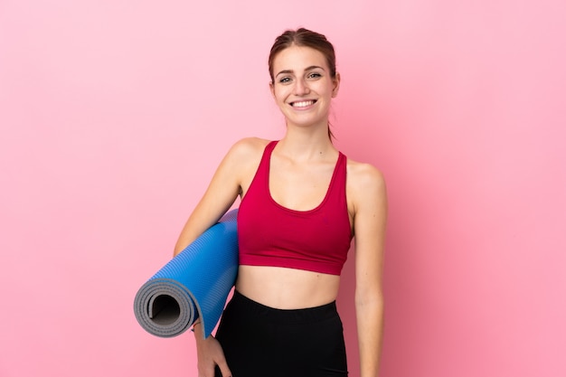 Jeune femme sport sur mur rose isolé avec un tapis et souriant