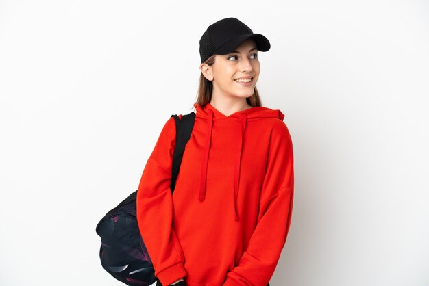 Jeune femme de sport avec sac de sport sur blanc pensant une idée tout en levant