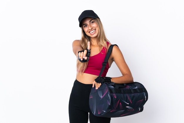 Jeune femme de sport avec sac de sport sur fond blanc isolé montrant et soulevant un doigt