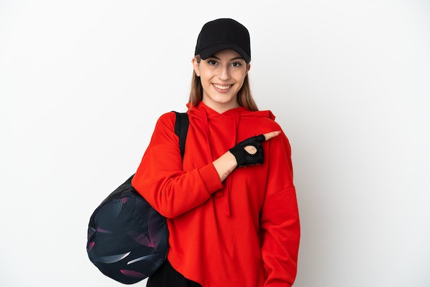 Jeune femme de sport avec sac de sport isolé sur un mur blanc pointant vers le côté pour présenter un produit