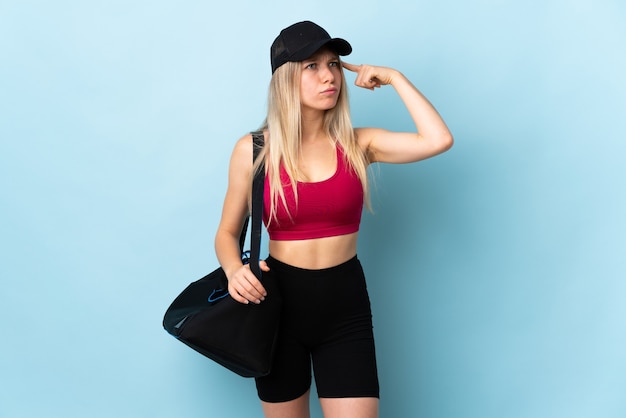 Jeune femme de sport avec sac de sport isolé sur mur bleu ayant des doutes et de la pensée