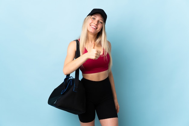 Jeune femme sport avec sac de sport isolé sur mur bleu donnant un coup de pouce geste