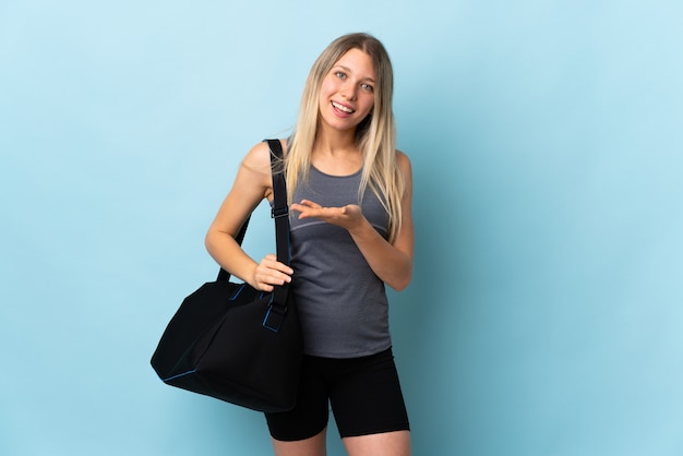 Jeune femme de sport avec sac de sport isolé sur mur bleu présentant une idée tout en regardant en souriant vers