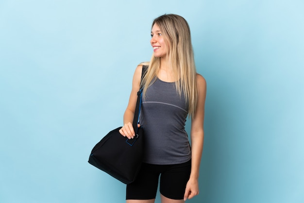 Jeune femme sport avec sac de sport isolé sur mur bleu à la recherche sur le côté