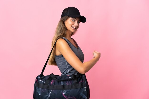 Jeune femme de sport avec sac de sport isolé sur un mur rose pointant vers l'arrière