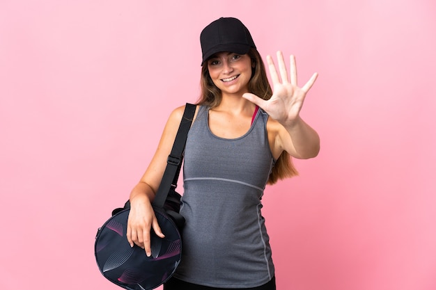 Jeune femme de sport avec sac de sport isolé sur rose comptant cinq avec les doigts