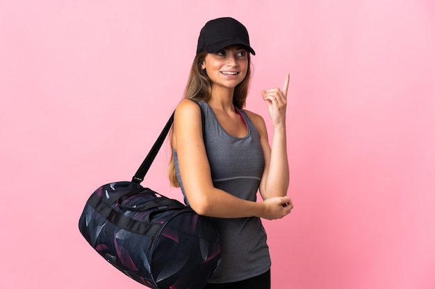 Jeune femme de sport avec sac de sport isolé sur rose pointant vers le haut une excellente idée