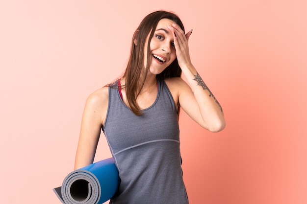 Jeune femme sport avec tapis sur mur isolé avec expression faciale choquée