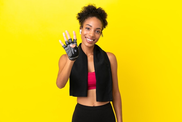 Jeune femme sportive africaine isolée sur fond jaune heureuse et comptant quatre avec les doigts