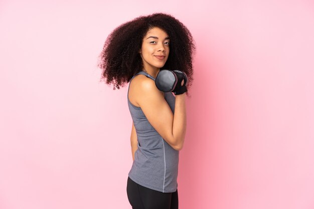 Jeune femme sportive afro-américaine isolée sur rose faisant de l'haltérophilie