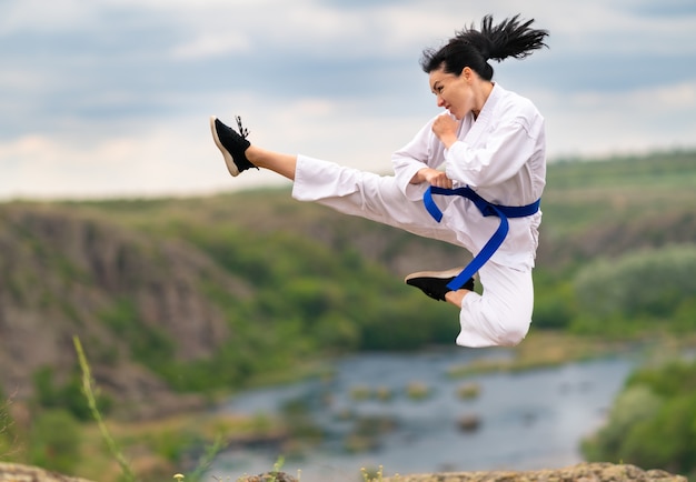 Jeune femme sportive agile pratiquant le kickboxing sautant dans les airs avec la jambe étendue et les mains serrées