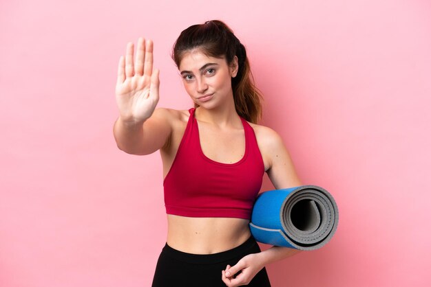 Jeune femme sportive allant à des cours de yoga tout en tenant un tapis faisant un geste d'arrêt