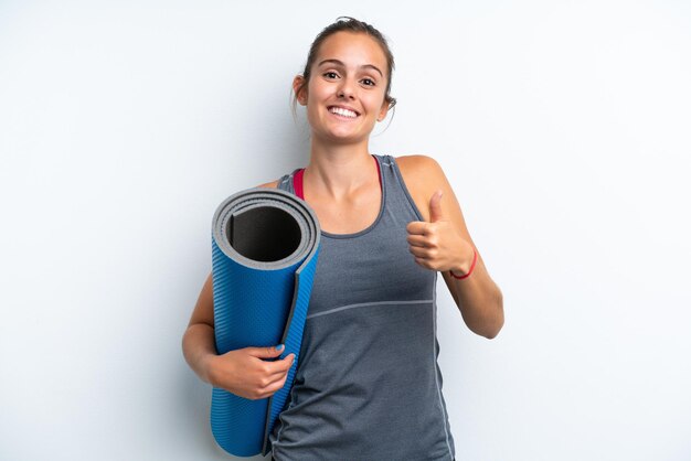 Jeune femme sportive allant à des cours de yoga tout en tenant un tapis isolé sur fond blanc en donnant un geste du pouce levé