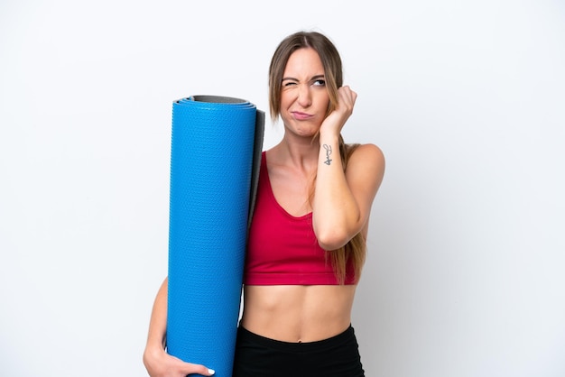 Jeune femme sportive allant à des cours de yoga tout en tenant un tapis isolé sur fond blanc frustré et couvrant les oreilles