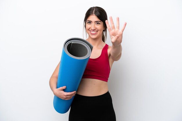 Jeune femme sportive allant à des cours de yoga tout en tenant un tapis isolé sur fond blanc heureux et en comptant quatre avec les doigts