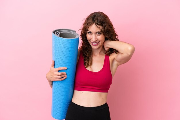 Jeune femme sportive allant à des cours de yoga tout en tenant un tapis isolé sur fond rose en riant