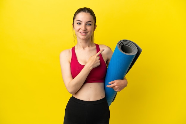 Jeune femme sportive allant à des cours de yoga tout en tenant un tapis pointant sur le côté pour présenter un produit