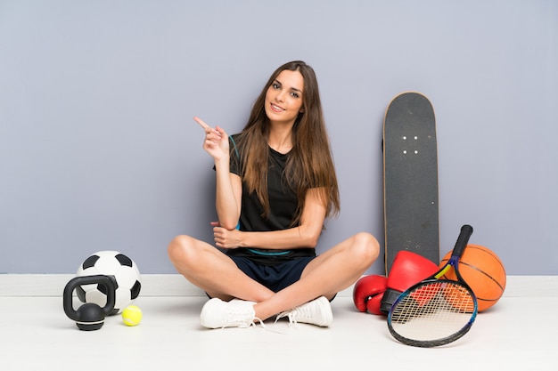 Jeune femme sportive assis sur le sol, pointant le doigt sur le côté