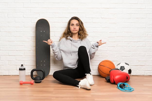 Jeune femme sportive assise sur le sol en montrant les latéraux ayant des doutes