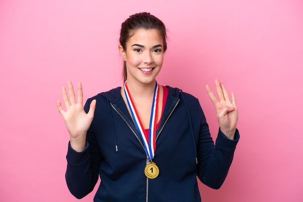 Jeune femme sportive brésilienne avec des médailles isolées sur fond rose comptant neuf avec les doigts