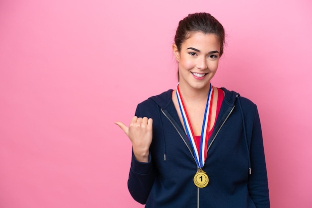 Jeune femme sportive brésilienne avec des médailles isolées sur fond rose pointant vers le côté pour présenter un produit