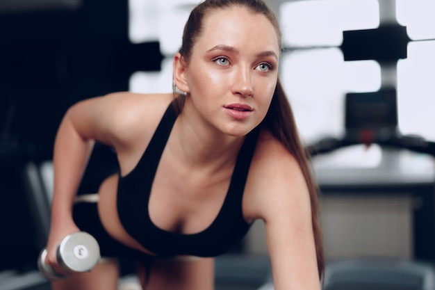 Jeune femme sportive brune exerçant avec haltère dans une salle de sport