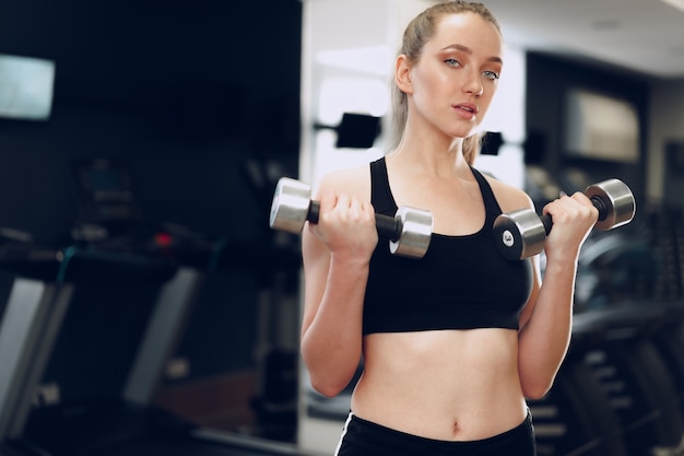 Jeune femme sportive brune exerçant avec haltère dans une salle de sport