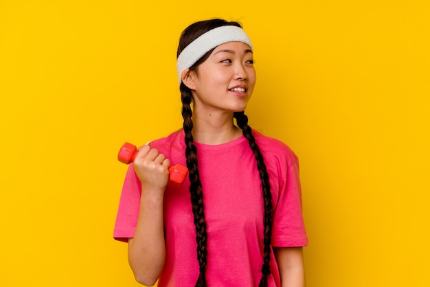 Jeune femme sportive chinoise isolée sur fond jaune regarde de côté souriante, gaie et agréable.