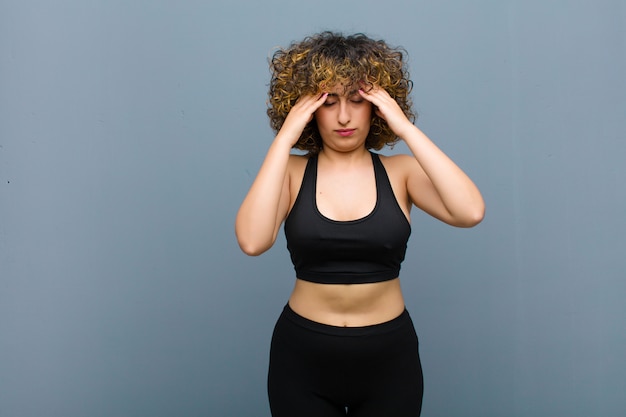 Jeune femme sportive à la concentration, réfléchie et inspirée, remue-méninges et imaginer avec les mains sur le front sur le mur gris