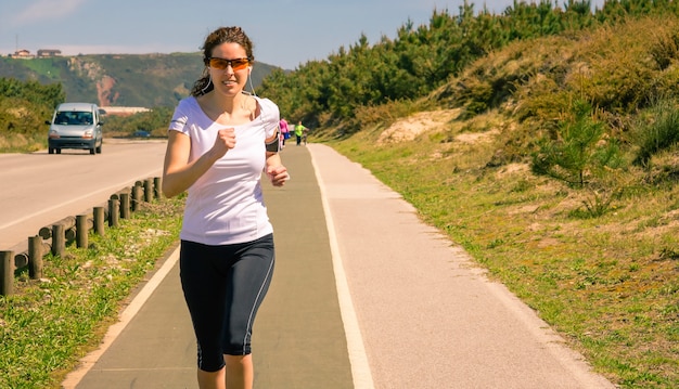 Jeune femme sportive avec des écouteurs écoutant de la musique depuis son smartphone tout en courant sur une piste à l'extérieur. Concept de mode de vie sain moderne.