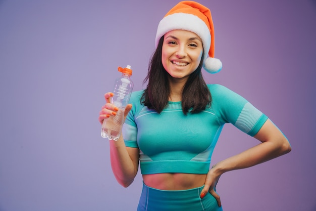 Jeune Femme Sportive En Formation De Chapeau De Noël Et Eau Potable, Isolée Sur Fond De Studio Dégradé à La Lumière Du Néon. Sport Moderne, Action, Mouvement, Concept De Jeunesse.