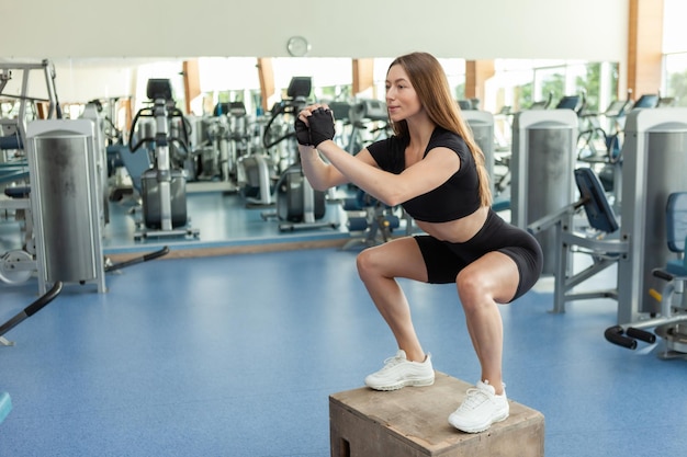 Une jeune femme sportive en forme fait des sauts de boîte dans une salle de sport. Entraînement croisé