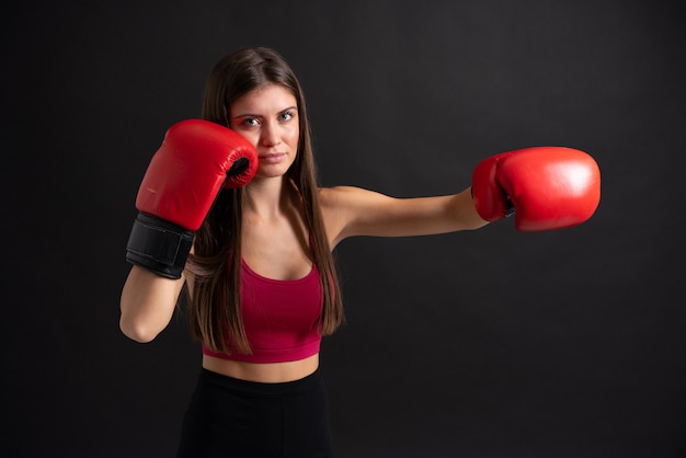 Jeune femme sportive avec des gants de boxe sur noir isolé