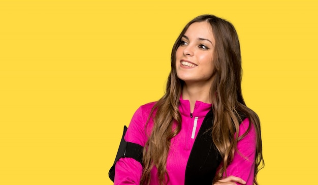 Jeune femme sportive gardant les bras croisés en souriant sur un mur jaune isolé
