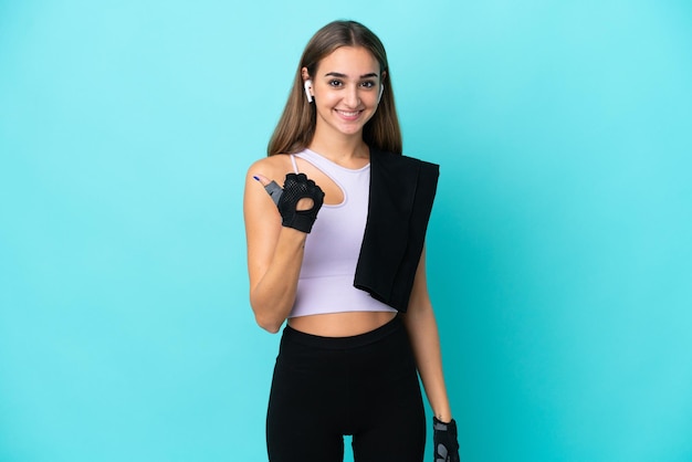 Jeune femme sportive isolée sur fond bleu pointant sur le côté pour présenter un produit