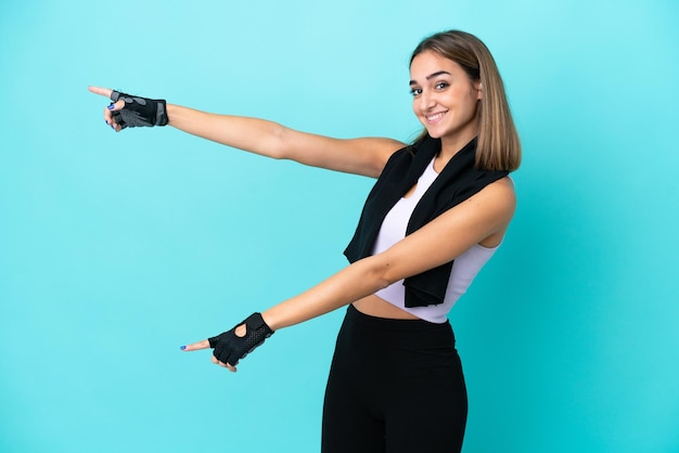 Jeune femme sportive isolée sur fond bleu pointant le doigt sur le côté et présentant un produit