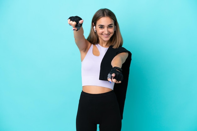 Jeune femme sportive isolée sur fond bleu pointe le doigt vers vous en souriant