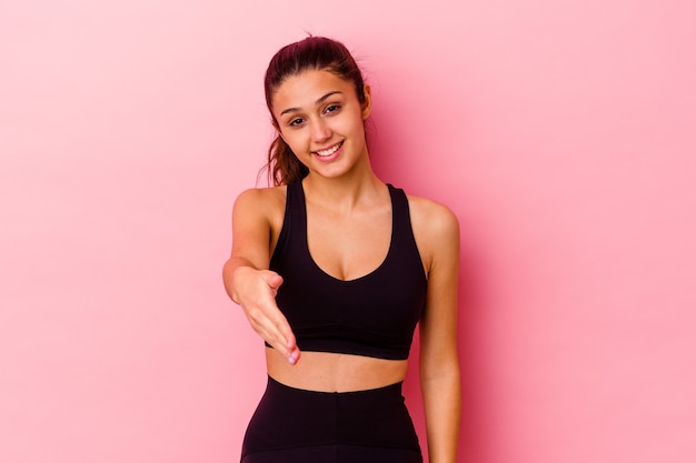 Jeune femme sportive isolée sur un mur rose qui s'étend la main à l'avant en geste de salutation