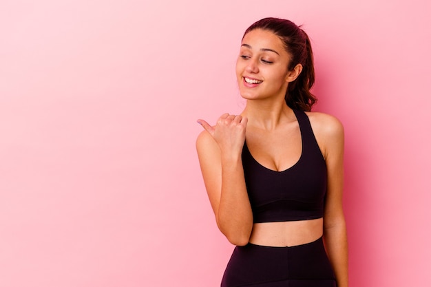 Jeune femme sportive isolée sur les points de mur rose avec le pouce, riant et insouciant