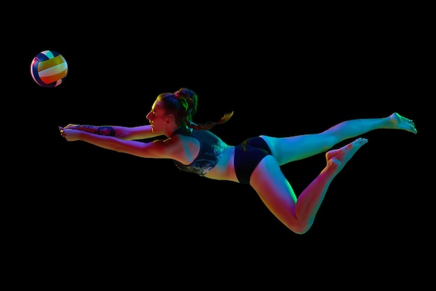 Jeune femme sportive joueur de volley-ball frappant la balle en mouvement et tombant sur fond noir de studio dans la lumière du néon Concept de compétition sportive professionnelle santé passe-temps action annonce