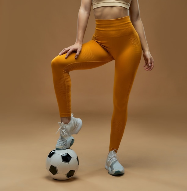 Jeune femme sportive mettant la jambe sur le ballon de football