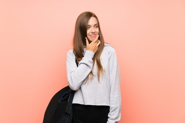 Jeune femme sportive sur un mur rose isolé, pensant à une idée