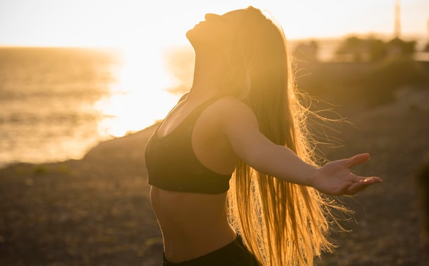 Une jeune femme sportive ouvrant les bras tendus contre un magnifique coucher de soleil doré avec vue sur la côte de l'océan Concept de bonheur et de mode de vie sain et actif Routine d'entraînement quotidienne
